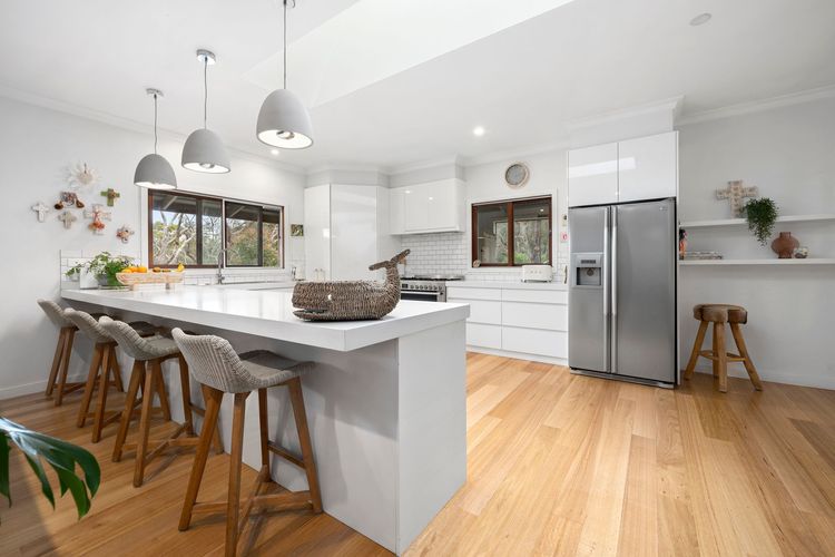 All-white full kitchen with a long benchtop and 3 pendant lights, giving the place a modern and elegant appeal.