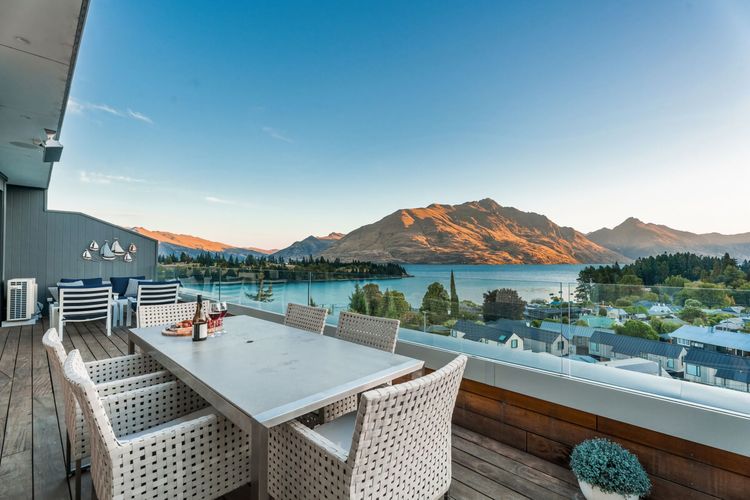 Expansive outdoor balcony with dining table, outdoor heaters, hanging chair, and incredible lake and mountain views.