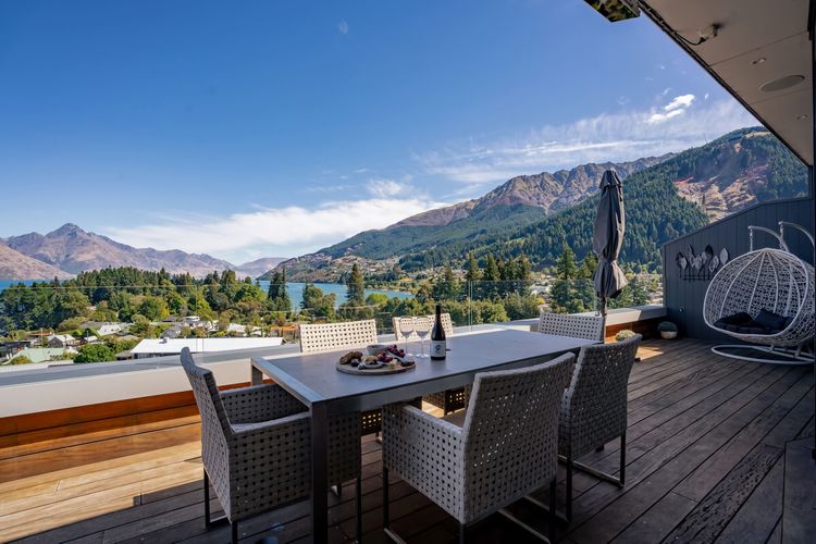 Expansive outdoor balcony with dining table, outdoor heaters, hanging chair, and incredible lake and mountain views.