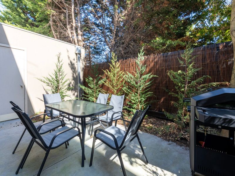 Private outdoor courtyard featuring a dining table set surrounded by lush greenery and a fence.