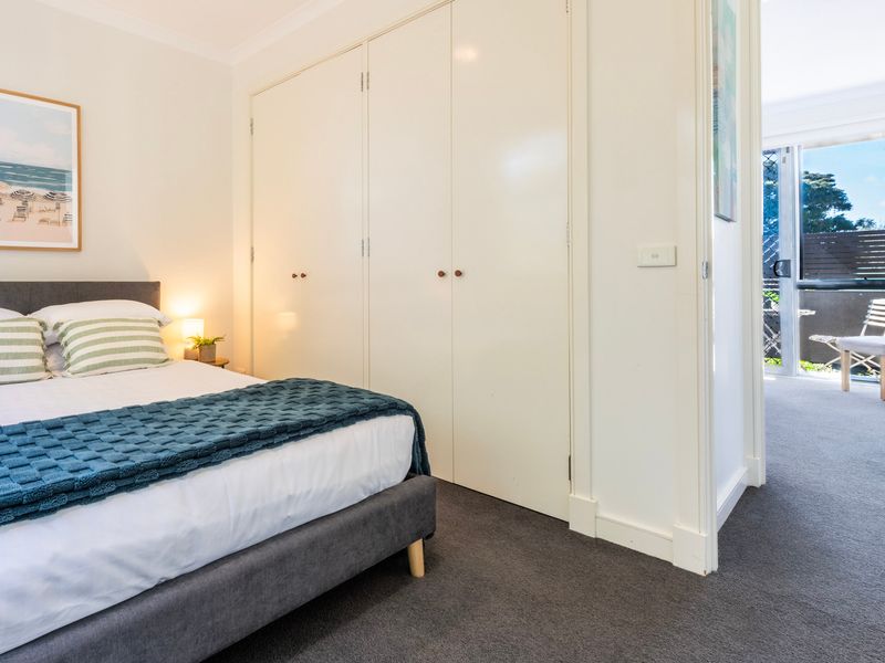 Cozy secondary bedroom featuring a well-made bed and white wardrobe doors leading out to the hallway.