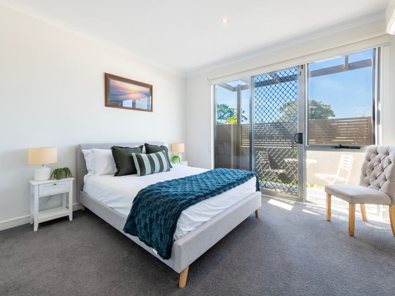 Bright bedroom featuring crisp white bedding, teal accent throws, and large windows bringing in natural light.