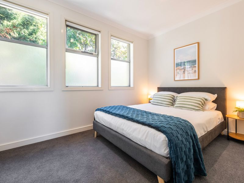 Spacious guest bedroom styled with a teal throw blanket, artwork, and ample natural light.