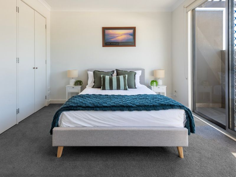 Alternative bedroom view showcasing the neat bed setup, a bedside table with a lamp, and built-in wardrobes.