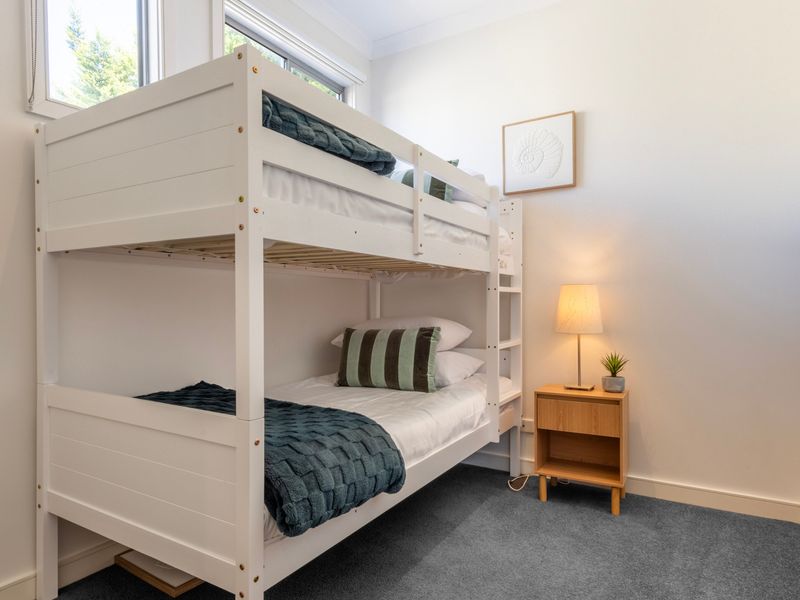 Children's bunk room featuring a white wooden bunk bed structure, striped bedding, and a bedside nightstand.