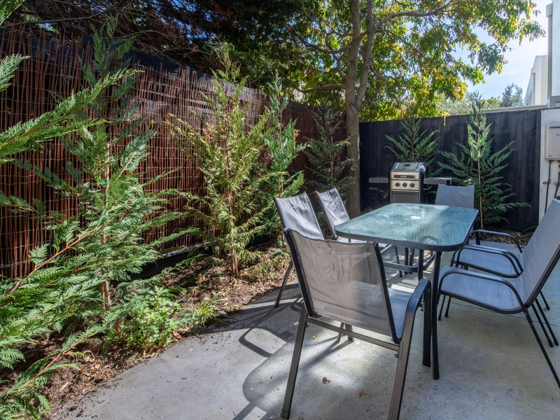 Covered backyard garden patio featuring outdoor seating and dense surrounding plants.