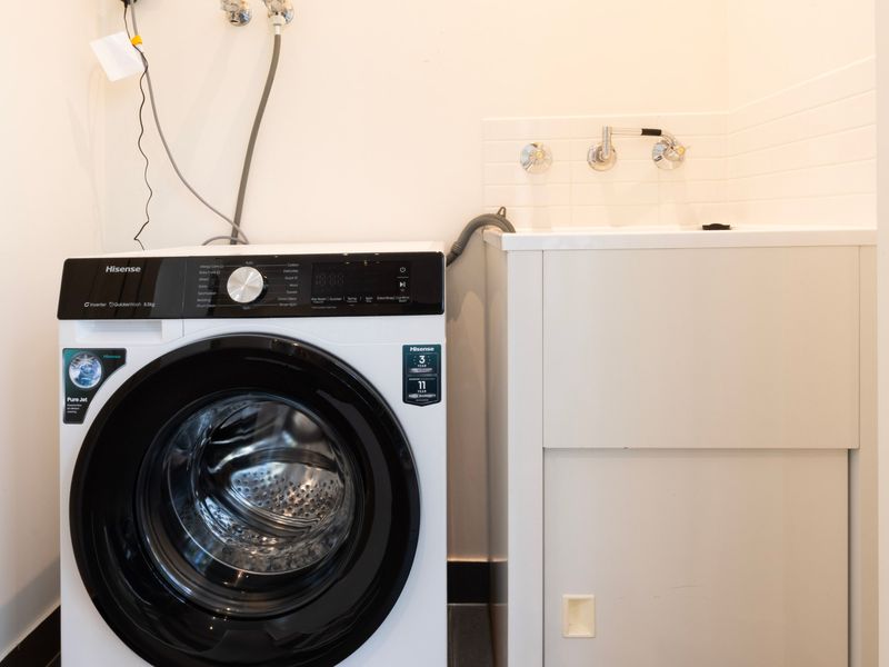 Functional laundry nook equipped with a front-load washing machine and clean white cabinetry.