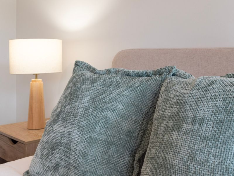 Close-up of textured teal throw pillows on a bed with a warm bedside lamp.