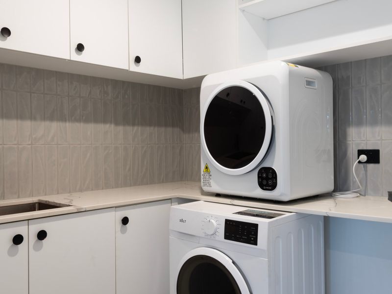 Laundry setup with a white washing machine unit placed beneath counter shelving.