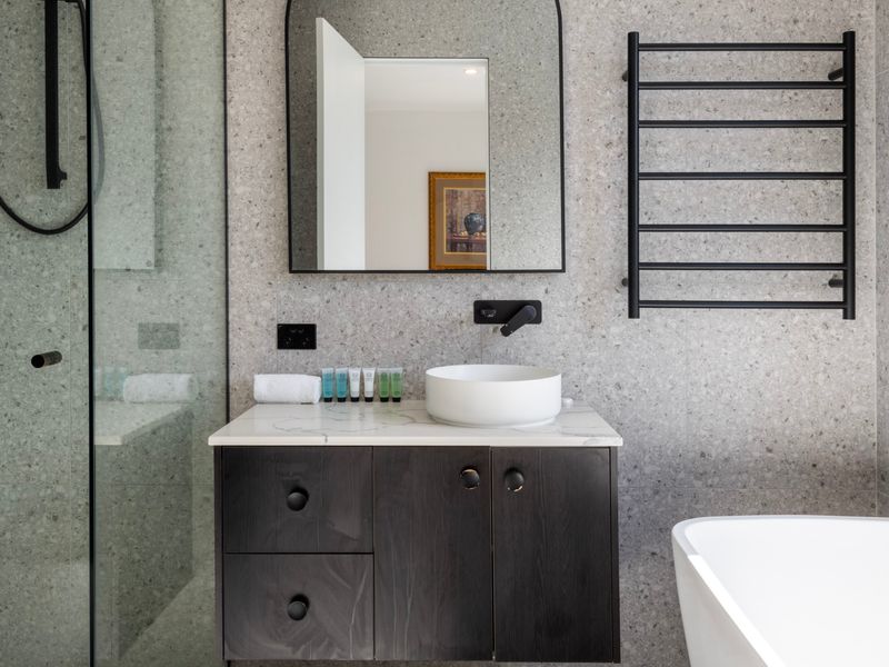 Modern bathroom vanity featuring a dark cabinet, white sink basin, and a wall-mounted mirror.