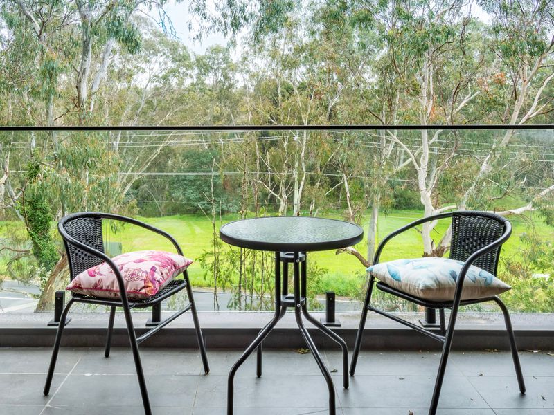 Outdoor patio balcony featuring a small table and black wire chairs overlooking greenery.