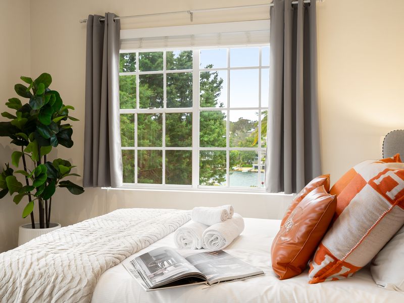 Bright bedroom with a bed featuring orange accent pillows and a large window.