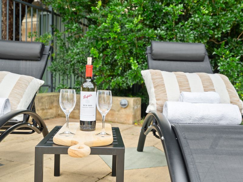 Outdoor lounge chairs by the poolside set up with wine glasses for relaxing.