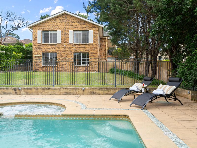 Poolside view facing the brick home and surrounding green trees.