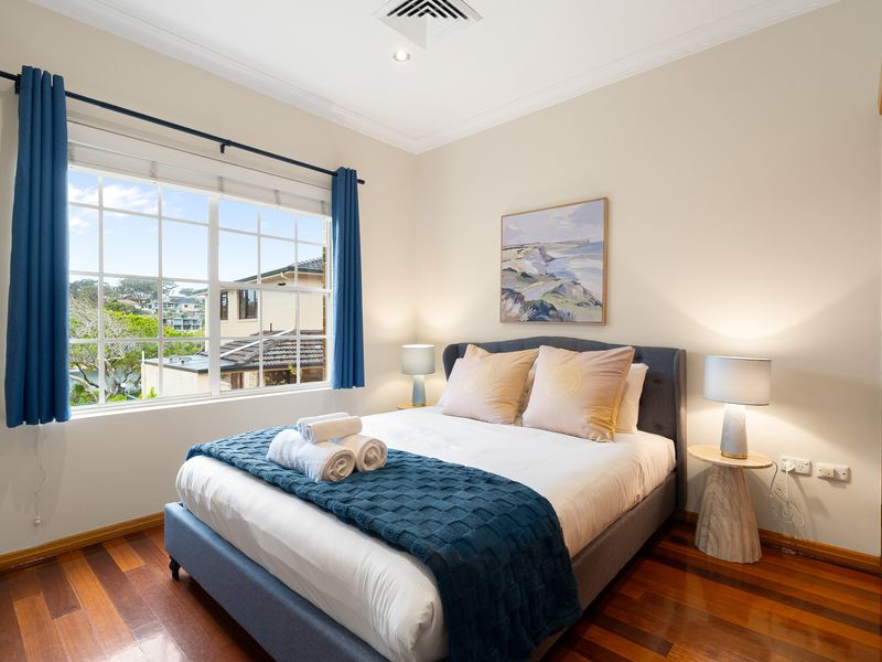 Bedroom with a neatly made bed, blue throw blanket, and window view.