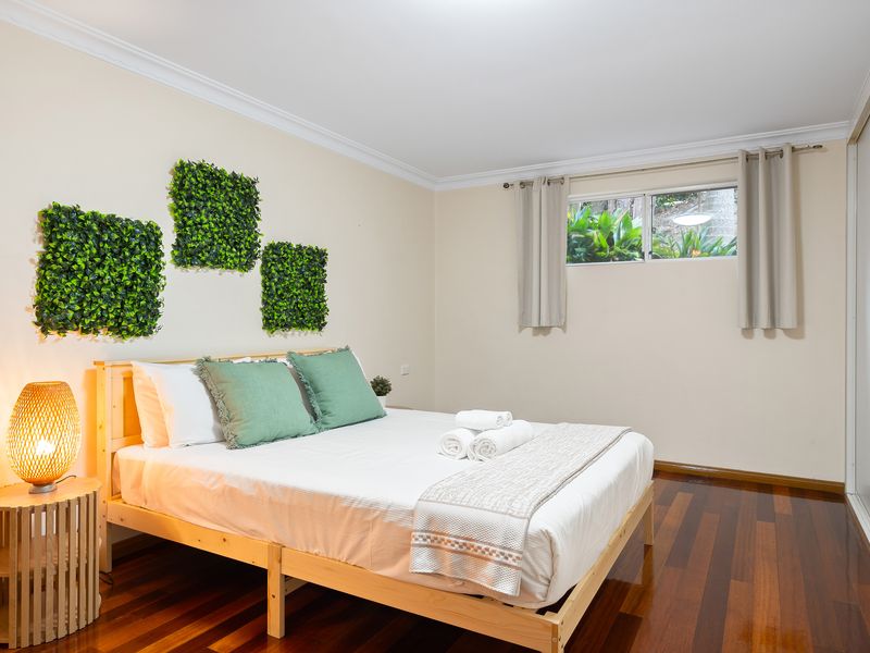 Cozy bedroom featuring soft green accents, wall plant decor, and a window view.