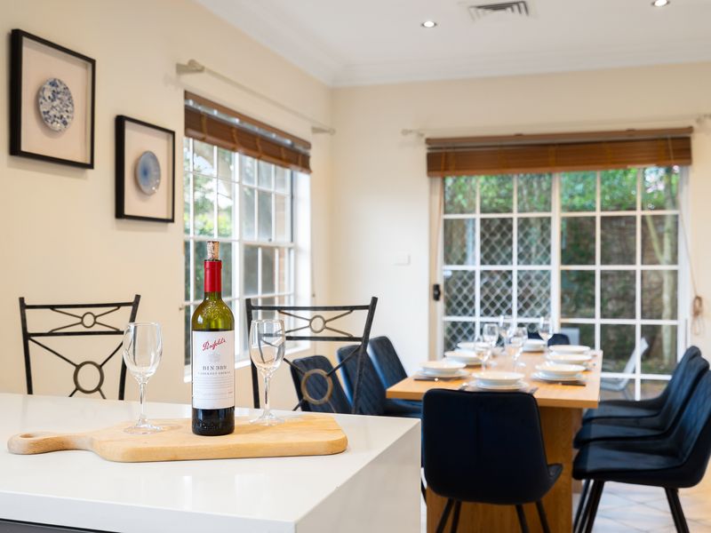 Dining table set near large windows overlooking the garden and trees.