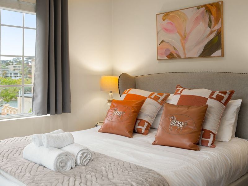 Guest bedroom setup with patterned pillows and large windows overlooking greenery.