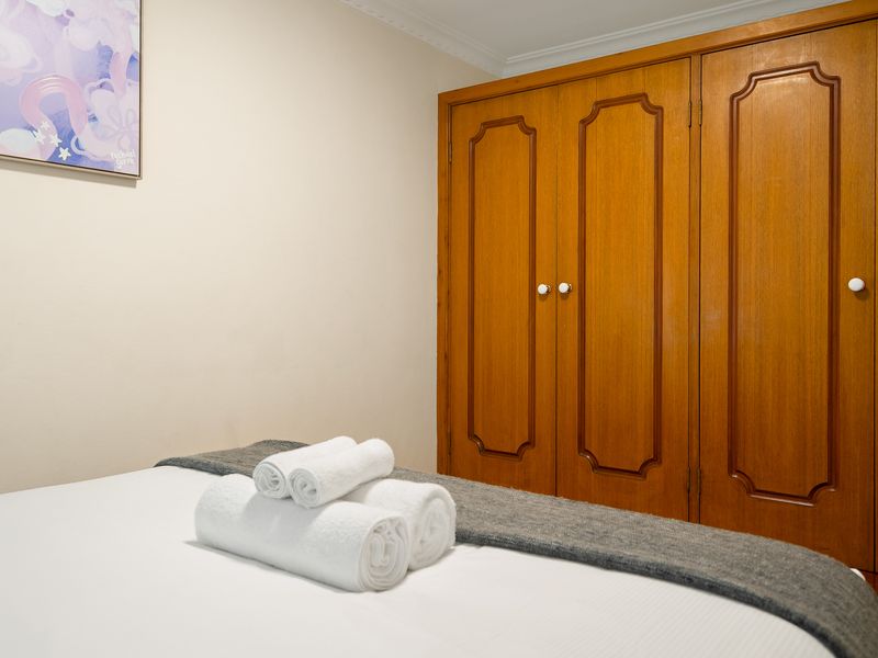 Bedroom with neat white bedding, a wooden wardrobe cabinet, and bright lighting.