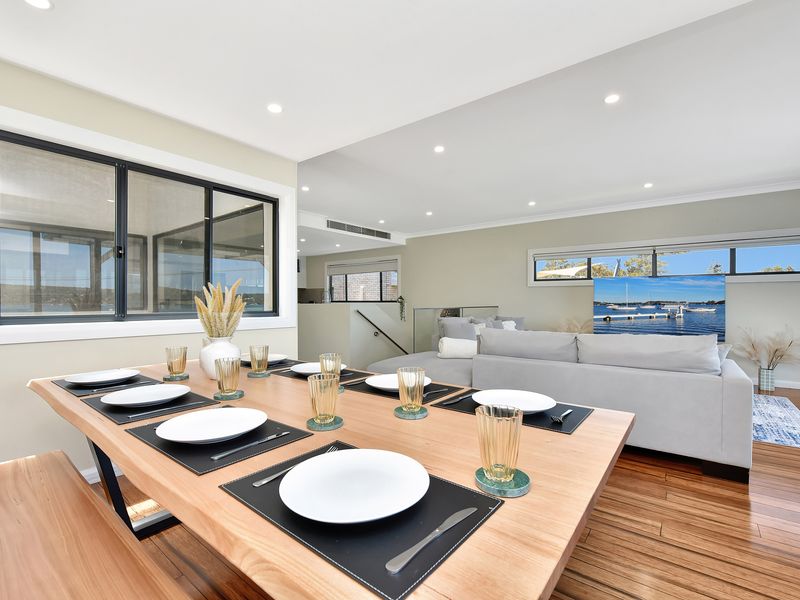 Modern open-plan dining and living area featuring a sleek wooden table set for six and a cozy lounge with water views.