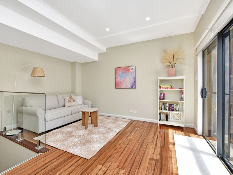 Bright and inviting living area featuring a cozy sofa, wooden flooring, and a private balcony. Accented with a soft rug, bookshelf, and modern décor for a relaxed, homely feel.