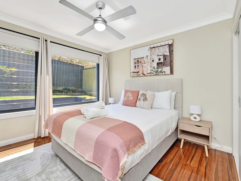 Bright and cozy bedroom featuring a comfortable queen bed, warm wooden floors, large windows with garden views, and stylish modern décor.