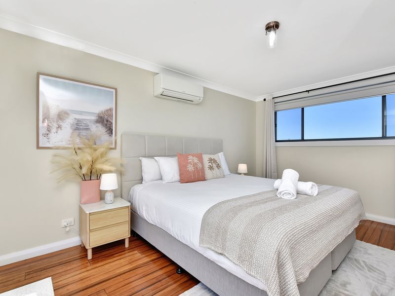 Bright and cozy bedroom featuring a comfortable queen bed with soft neutral bedding, stylish décor, and air conditioning.