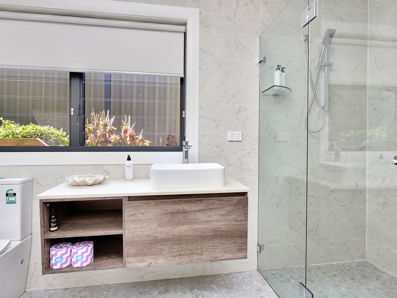 Bright and stylish bathroom featuring a floating vanity with wood finish, large window for natural light, and a sleek glass shower with modern fixtures.