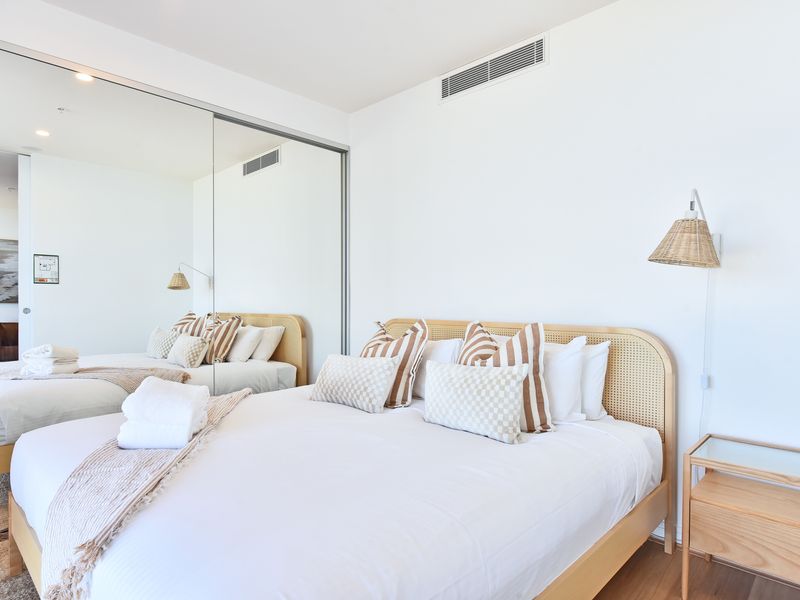 Modern coastal bedroom with soft tones, mirrored wardrobe and a cozy, relaxing atmosphere.