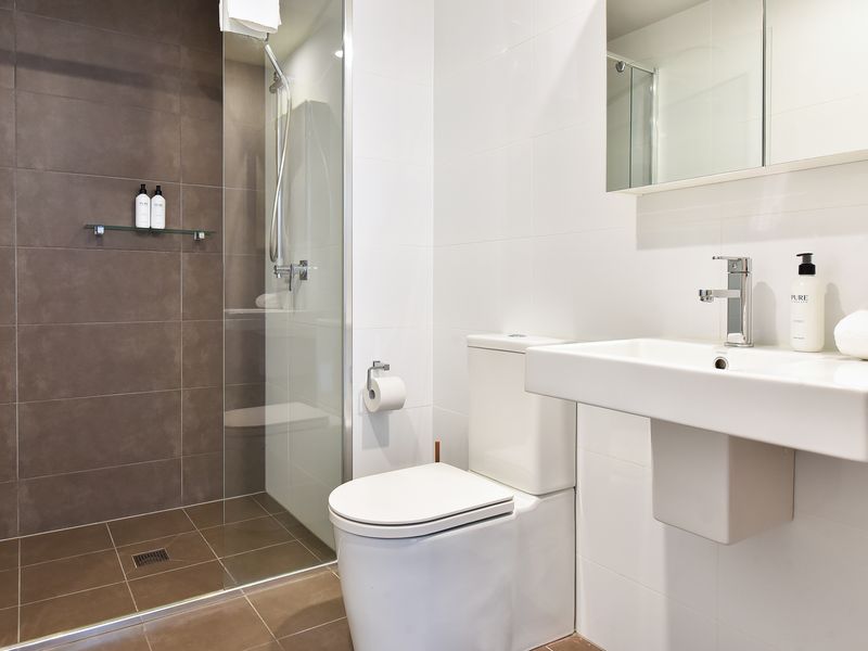 Features a spacious frameless glass shower with contemporary tiling, a stylish pedestal basin, and clean white fixtures.