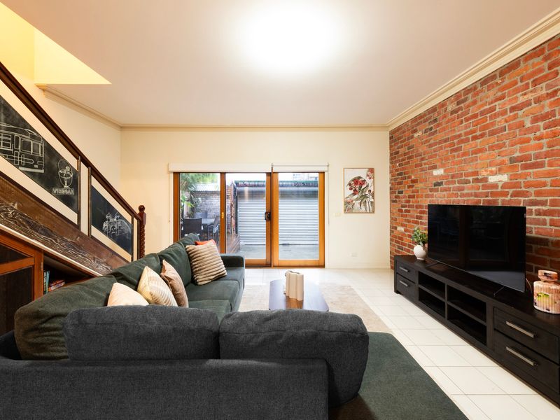 Exposed Brick Charm: Cozy living area featuring a striking brick feature wall and warm timber-framed glass doors.