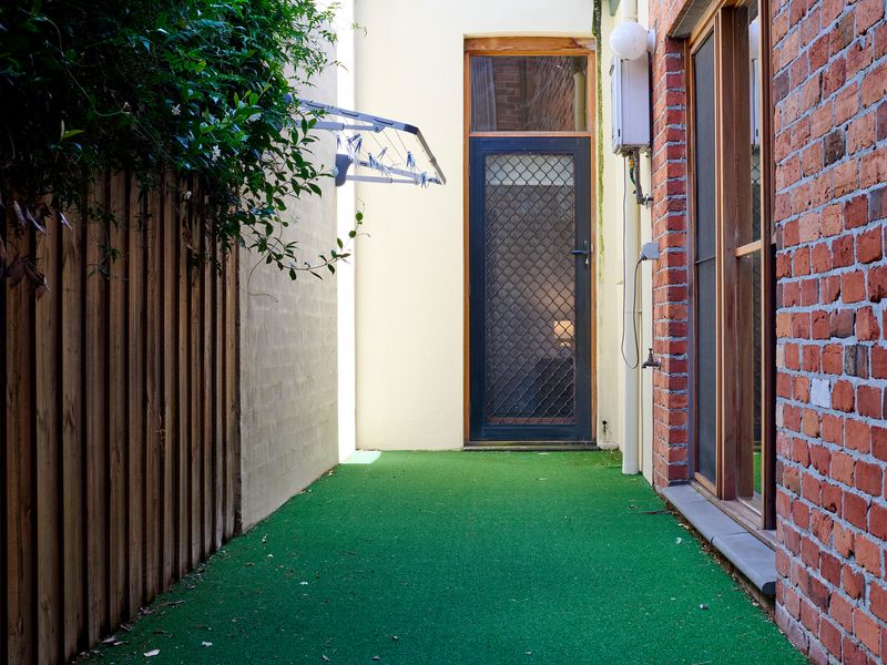 Private Green Pathway: Low-maintenance artificial turf strip framed by rustic exposed brick and warm timber paneling.