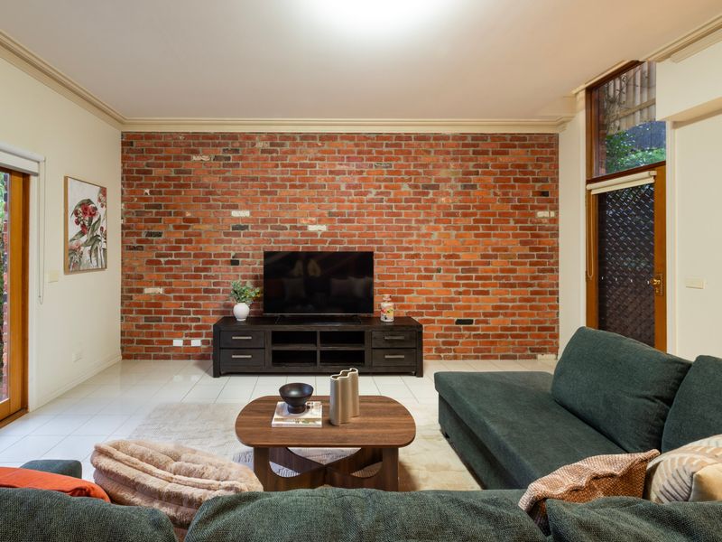 Industrial Living: Spacious lounge area anchored by a rustic brick accent wall and a plush green sectional.