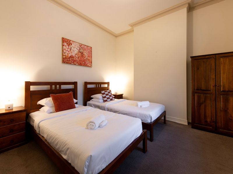 Twin Configuration: A spaciously arranged guest room featuring two matching single beds and rich timber cabinetry.