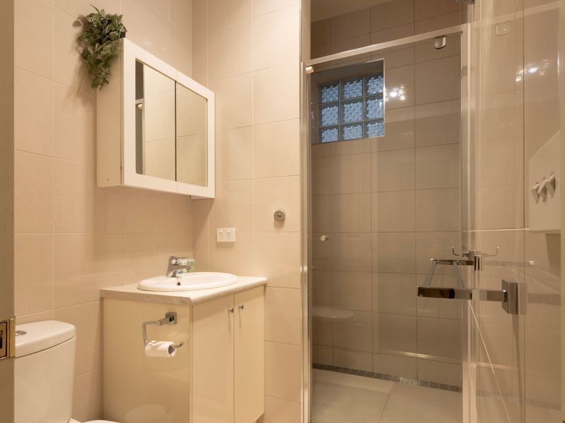 Compact Powder Room: Functional second bathroom featuring a neat vanity, mirrored storage cabinet, and glass shower screen.