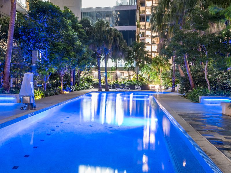 Communal Pool: The pool is set within a lush, tropical garden environment with numerous trees, palms, and foliage, creating a private, oasis-like feel.