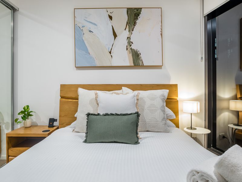 Bedroom 2: Sleep in Scandinavian Style. This designer bed features a beautifully curved natural timber headboard and frame. The crisp, clean white linen is dressed with five plump pillows.