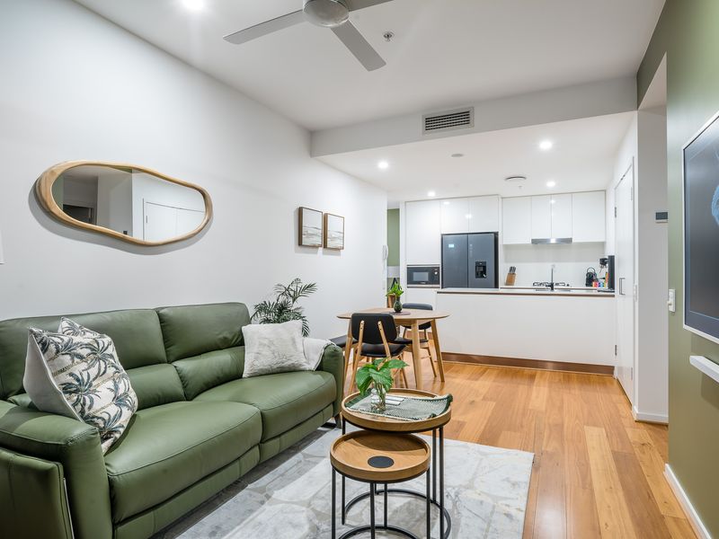 Living Room and Kitchen: Sink into the bespoke olive-green sofa for an evening of relaxation. Your compact but fully-equipped kitchen features high-gloss white cabinetry and all the essentials, including a large black refrigerator.