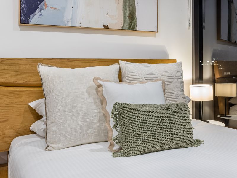 Bedroom 2: Sleep in Scandinavian Style. This designer bed features a beautifully curved natural timber headboard and frame. The crisp, clean white linen is dressed with five plump pillows.