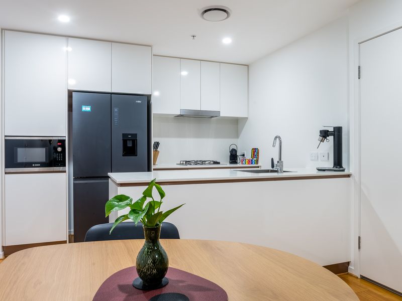 Gourmet Appliances: The kitchen is anchored by a sleek, large black refrigerator with a built-in water/ice dispenser. A microwave is integrated into the surrounding white cabinetry.