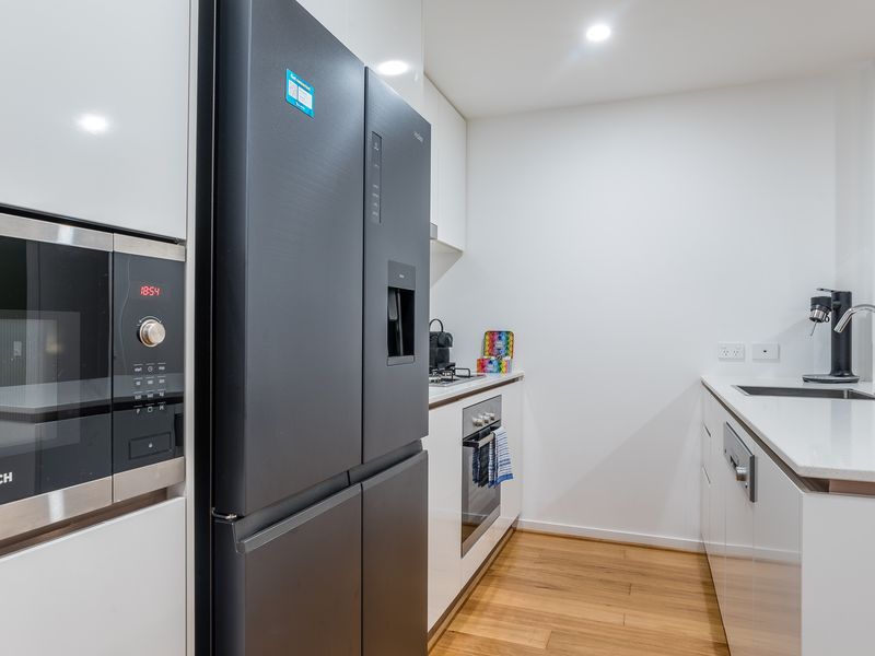 Gourmet Appliances: The kitchen is anchored by a sleek, large black refrigerator with a built-in water/ice dispenser. A microwave is integrated into the surrounding white cabinetry.