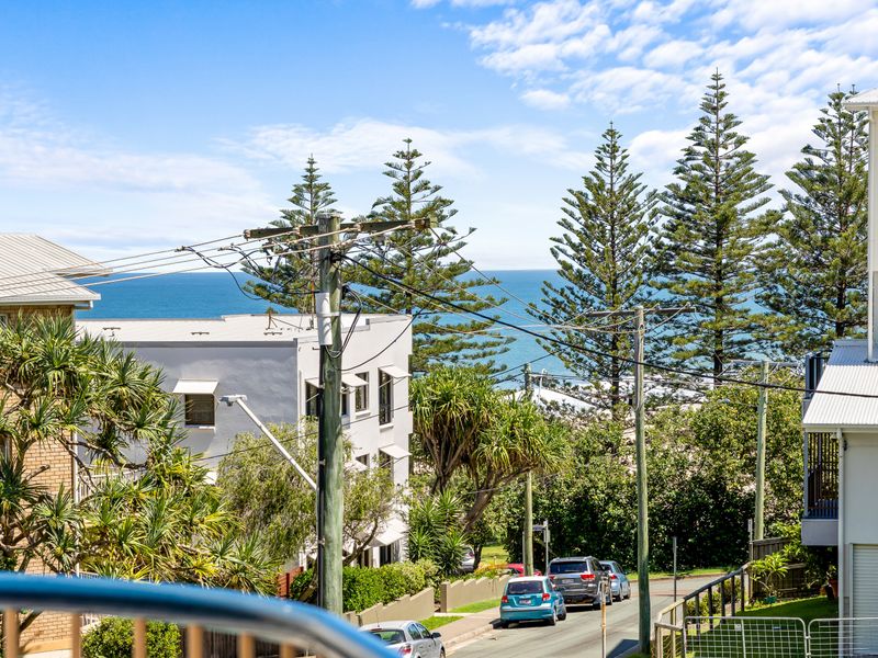 Relaxed neighborhood views with ocean glimpses. The balcony looks out over the local streetscape and nearby rooftops, offering clear views toward the ocean framed by coastal pine trees.