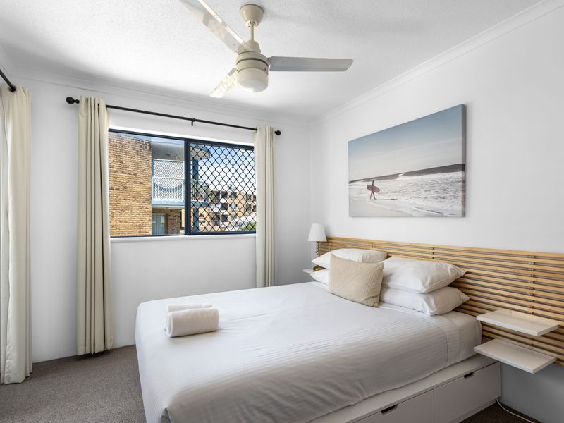 Bright and comfortable second bedroom featuring fresh bedding, a modern fan, and plenty of natural light.