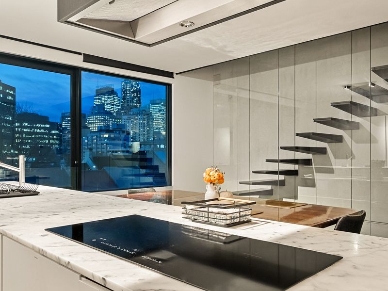 The space features a large kitchen island with a built-in cooktop, likely induction, and a sleek, minimalist design.