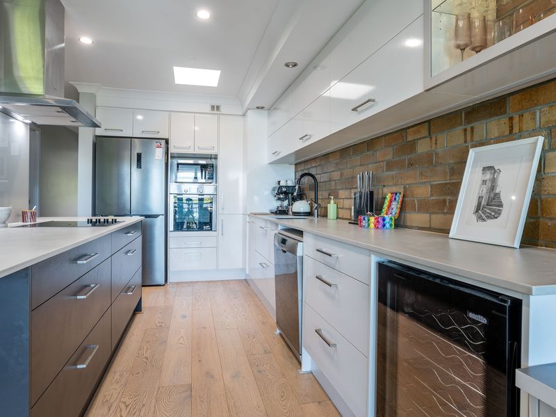 Fully equipped modern kitchen with stone benchtops, dishwasher, and brick splashback