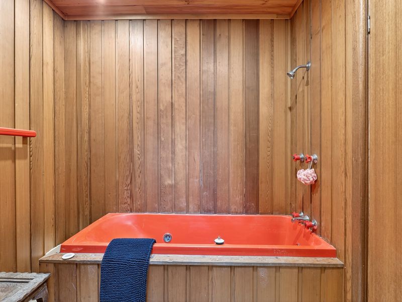 Bathroom featuring a deep red soaking tub set against warm timber paneling.