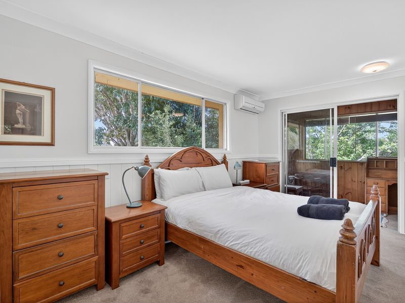 Bright master bedroom with timber furniture and large windows overlooking greenery.