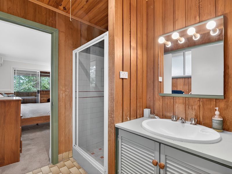 Bathroom with timber panelled walls, glass shower, and a wide vanity with mirror lighting.