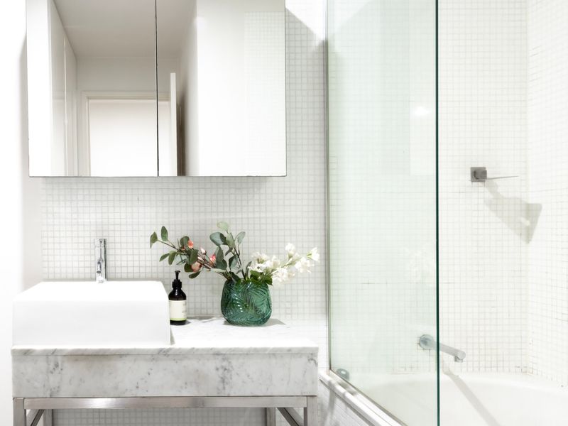 Sleek white design with a marble-style vanity, glass shower, and fresh greenery accents.