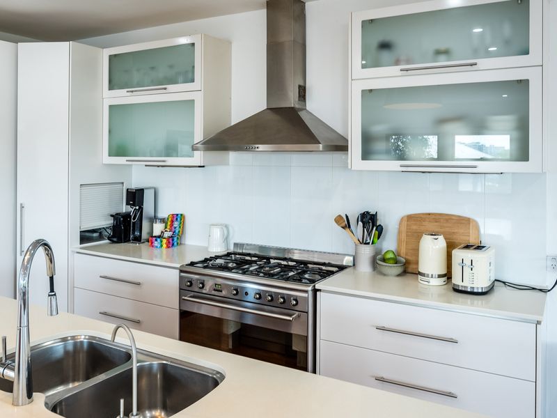 This gourmet kitchen is a chef's dream, featuring an extra-wide professional gas cooktop, sleek integrated cabinetry with frosted glass accents, and a large stone-topped island with a double stainless steel sink.